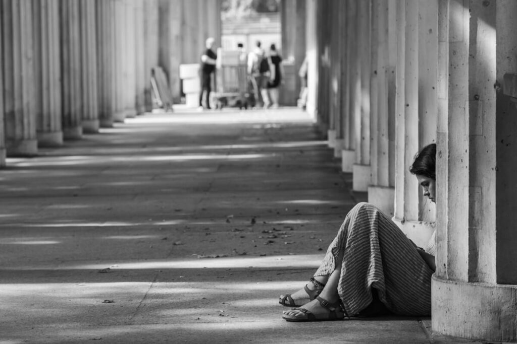 Girl sitting against a column at the 'Kolonnadenhof' on Museum Island in Berlin, looking at her mobile phone.